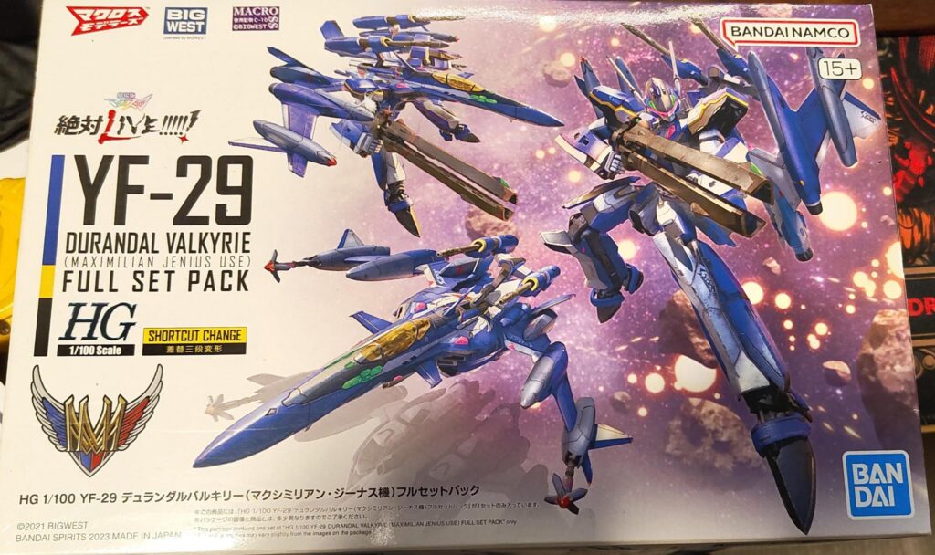Box art for the Bandai HG 1/100 YF-29 Durandal Valkyrie (Maximilian Jenius Use) Full Set Pack model kit from Macross. The artwork shows the blue Valkyrie mecha in both fighter jet and humanoid modes, equipped with large cannons, flying in space against a glowing starfield background. Logos for Bandai Namco, Bandai, Big West, and Macross are visible along with scale and age rating details.
